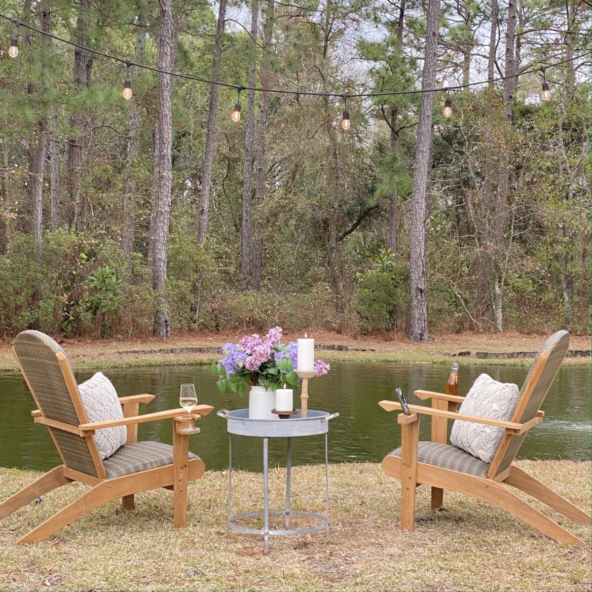 Beautiful Cambridge Casual Adirondack chairs next to a pond with a table in between them.