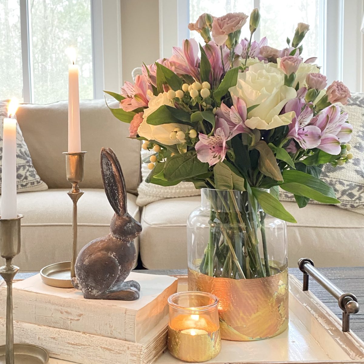 DIY gold leaf vase styled with Spring flowers on a tray with a bunny figurine, books, and candles.
