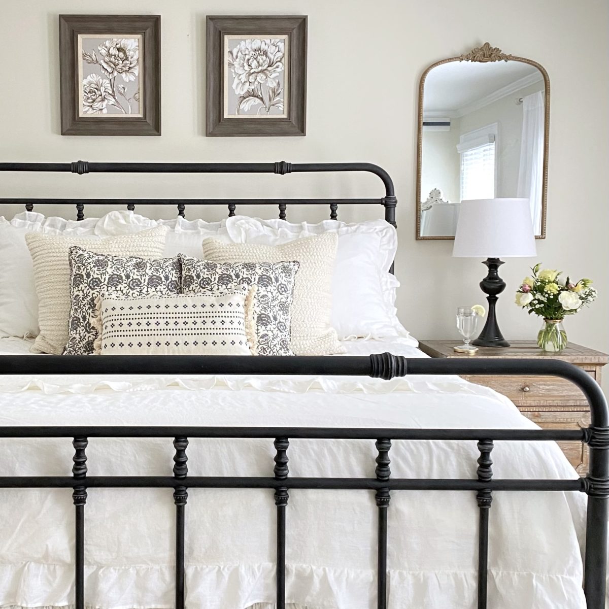 Simple summer bedroom with iron bed, white bedding, floral prints, and a mirror.