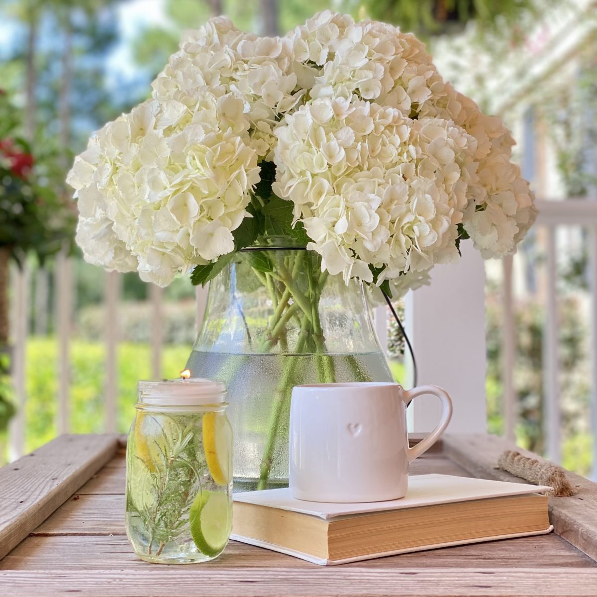 A DIY mason jar luminary on the porch coffee table with a book, a mug, and a vase of hydrangeas.