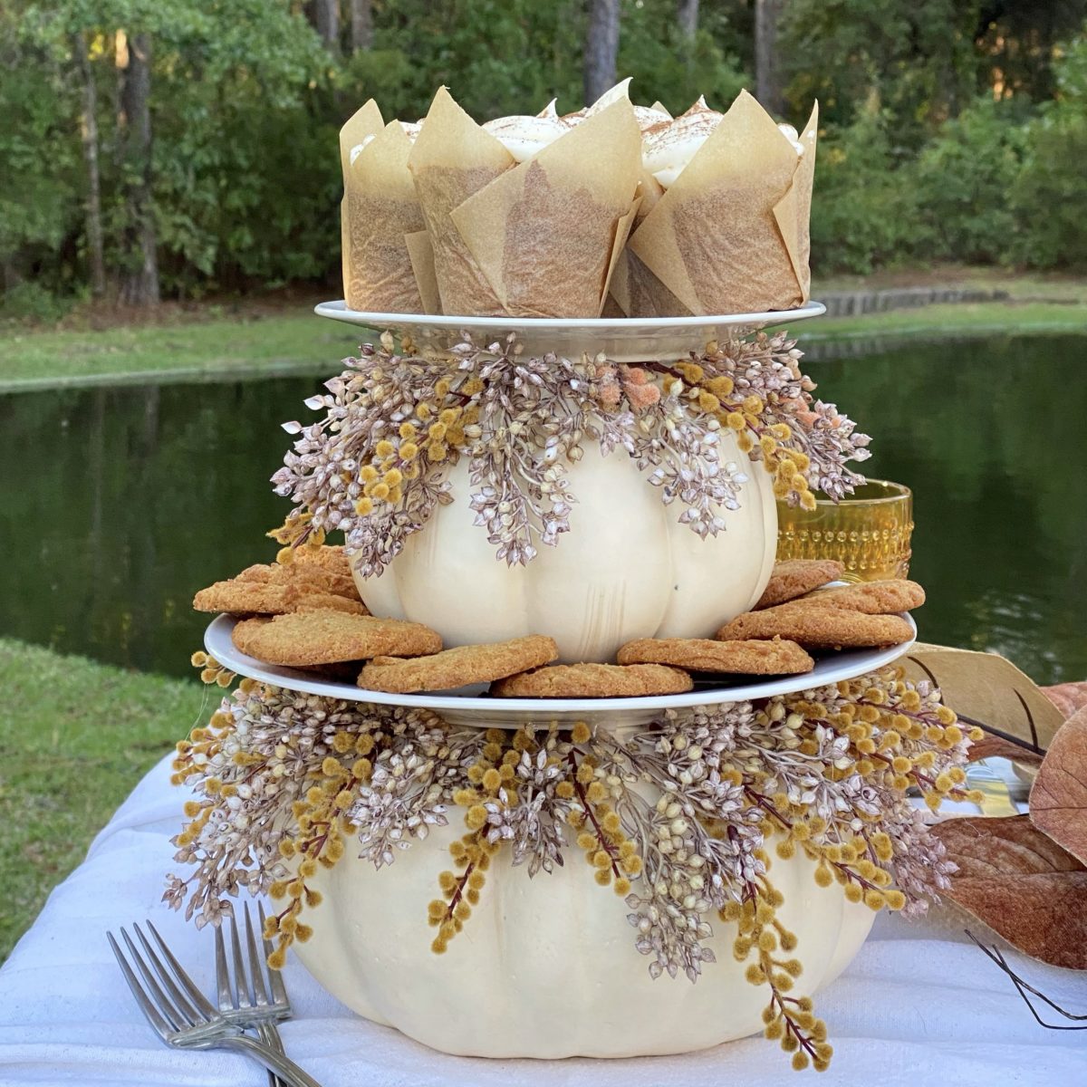 DIY Fall tiered tray with cookies and cupcakes displayed on it on a table by the pond.