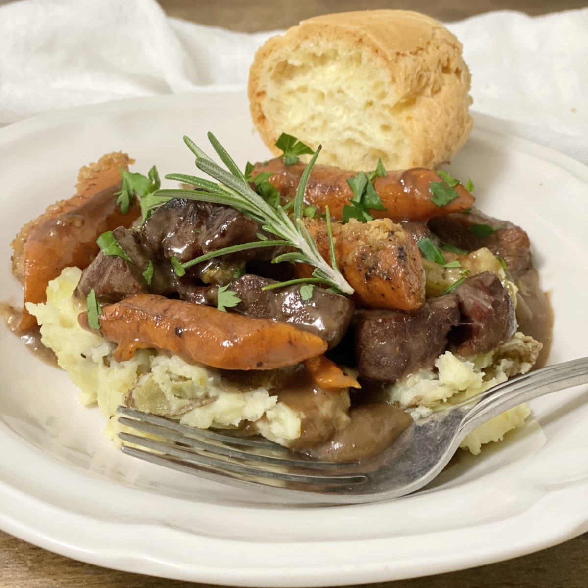 (No Peek) Oven Beef Stew over mashed potatoes in a white bowl with bread on the side.