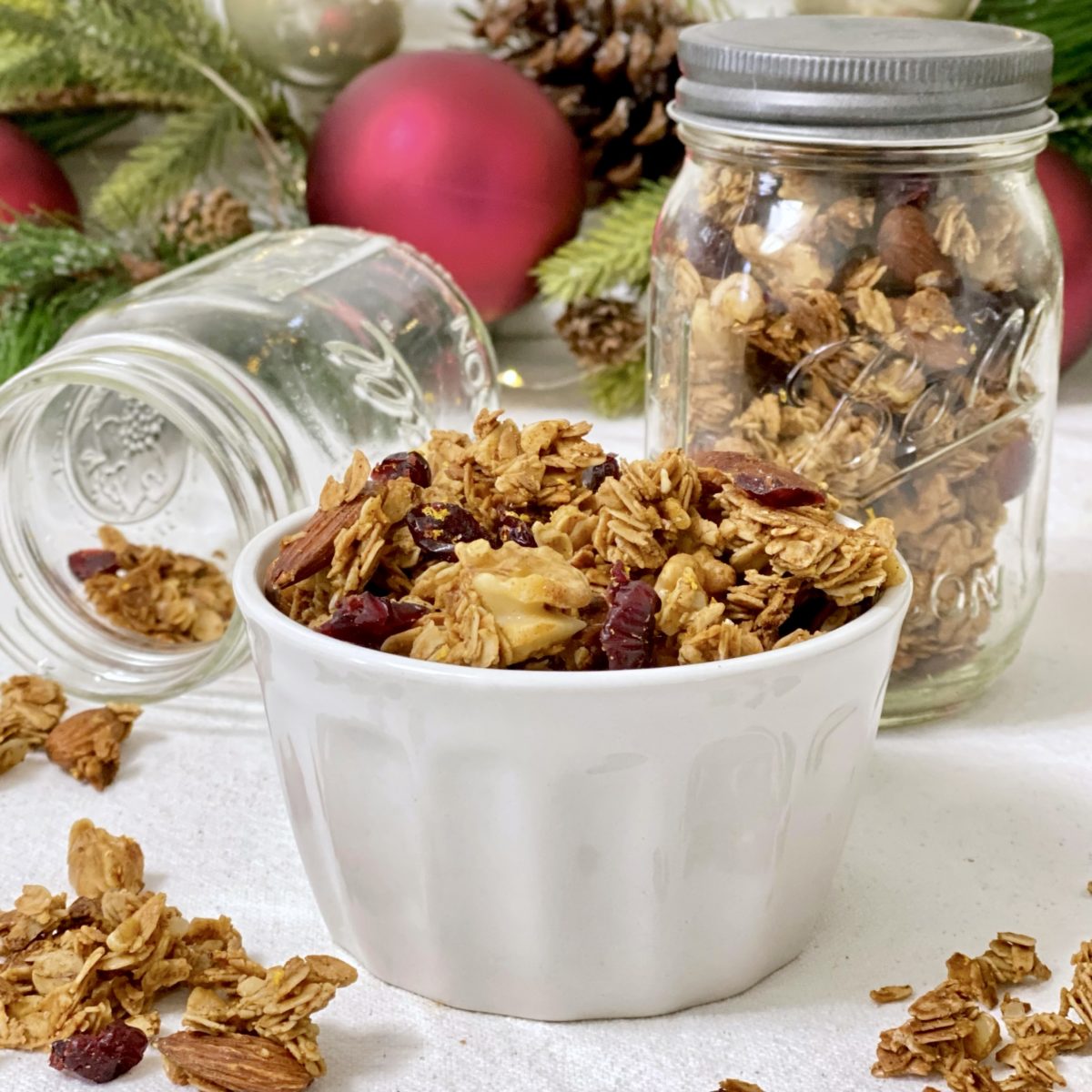 Merry Christmas Granola In a white dish with mason jars filled with granola in the background.