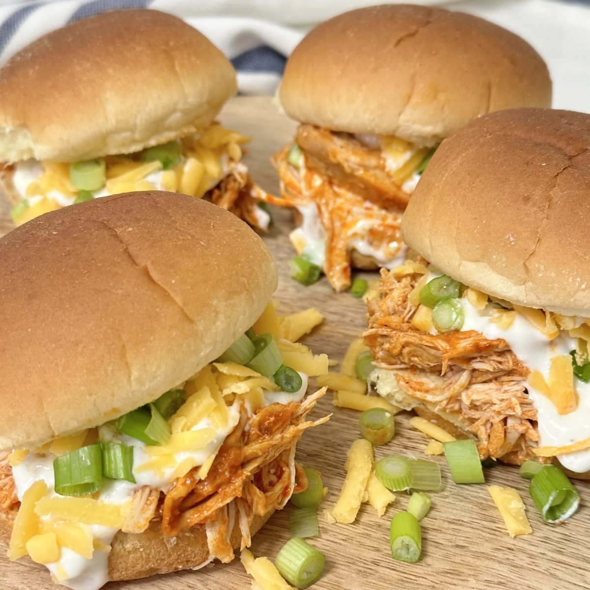 Slow Cooker Buffalo Chicken Sliders topped with ranch dressing, cheddar cheese, and sliced green onions.